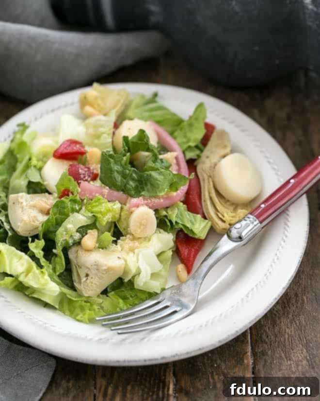A vibrant Italian Chopped Salad served on a white salad plate, accompanied by a stylish red-handled fork. The salad features crisp lettuce, colorful peppers, tender artichoke hearts, and hearts of palm.
