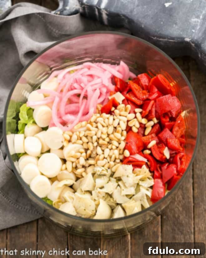 A large glass salad bowl filled with an abundance of fresh Italian Chopped Salad ingredients, ready to be tossed.