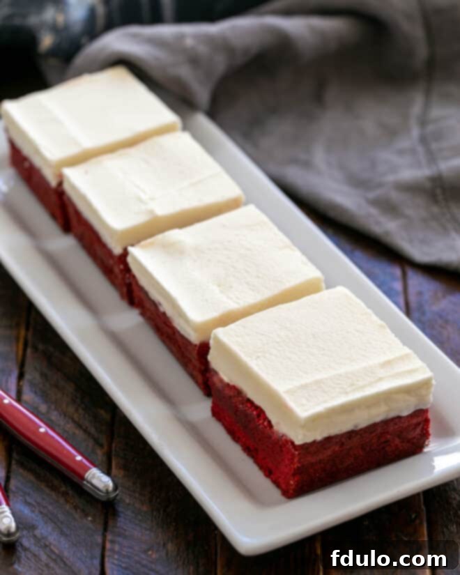 White Chocolate-Kissed Red Velvet Brownies 9 4 red velvet brownies on a white ceramic tray.