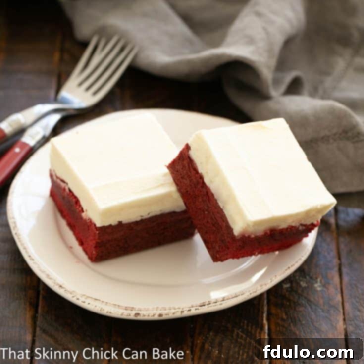 White Chocolate-Kissed Red Velvet Brownies 10 2 red velvet brownies on a round white dessert plate, covered in white chocolate icing.