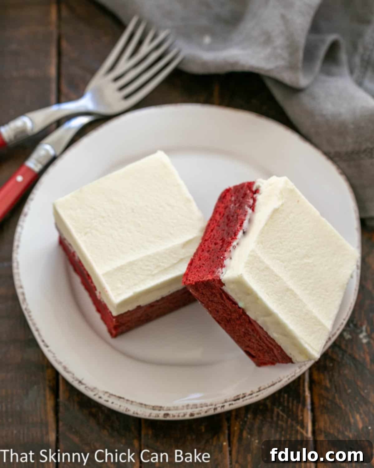 Red Velvet Brownies with White Chocolate Icing - Perfect for Valentine's Day or just because! Overhead view of 2 red velvet brownies on a round white plate, perfectly frosted and ready to eat.