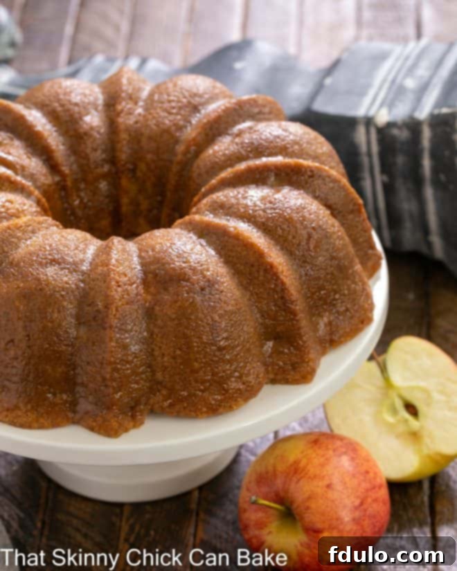 A stunning Apple Bundt Cake displayed on a white cake stand, flanked by two fresh, vibrant apples, highlighting its natural goodness.
