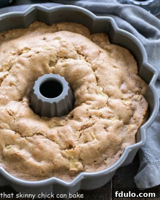 A freshly baked Apple Bundt Cake, still warm in its Bundt pan, just out of the oven, steam gently rising.