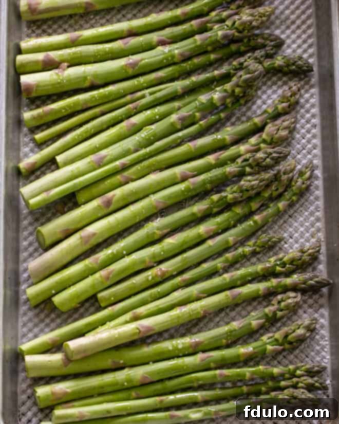 Fresh asparagus spears laid out on a sheet pan, drizzled with olive oil and seasoned with salt and pepper, ready for roasting.