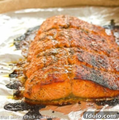 A close up of roasted Salmon on a foil lined baking sheet, showing its crispy skin and glazed top.