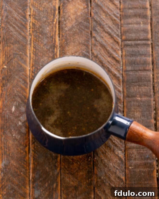 Close-up of maple syrup, mustard, vinegar, and thyme being mixed in a saucepan, simmering to create the glaze.