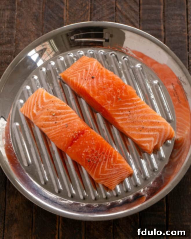 Fresh salmon fillets being patted dry with paper towels before being placed on an oiled grill pan.
