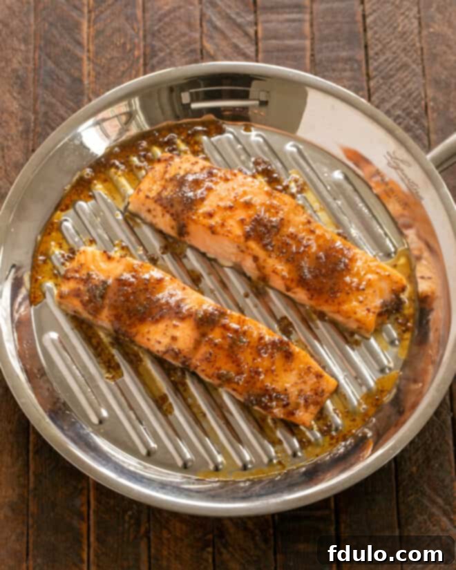 Salmon fillets on a baking sheet, seasoned with salt and pepper, and being brushed generously with the maple mustard glaze before roasting.