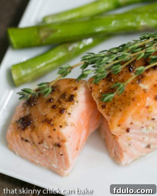 A close-up of Maple Mustard Glazed Salmon on a white plate, with the center exposed to show perfect medium-rare doneness, garnished with fresh thyme.