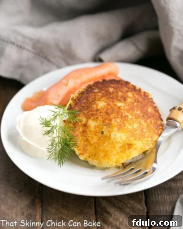 Gruyere Potato Cakes - Cheesy, herbed mashed potatoes fried to perfection Gruyere Potato Cakes served elegantly with smoked salmon, crème fraîche, and dill on a small white plate, perfect for an appetizer.