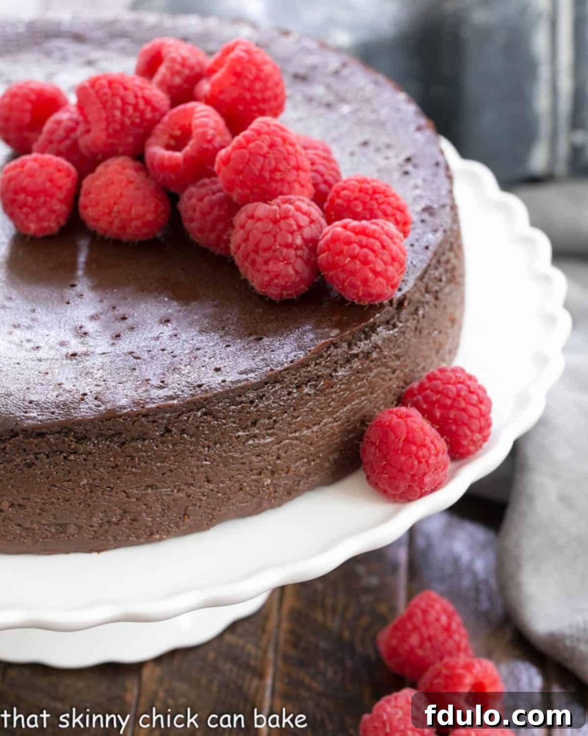 A stunning Flourless Chocolate Kahlua Cake adorned with fresh raspberries, sitting elegantly on a white cake stand.