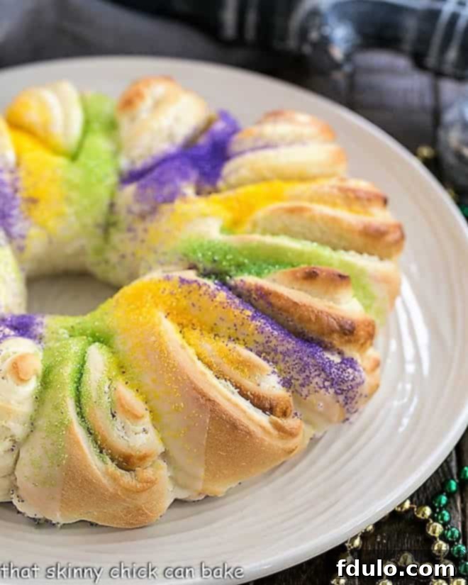 Easy King Cake with cream cheese filling on a white plate, adorned with vibrant Mardi Gras colors.
