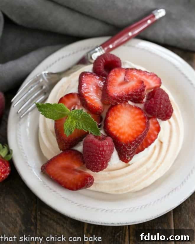 A mini pavlova on a round white plate, elegantly topped with whipped cream and fresh berries, ready to be enjoyed as a delightful individual dessert.