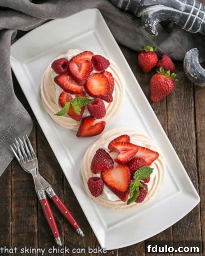 Overhead view of two meringue desserts on a white tray with two red handled forks, highlighting the tempting texture of mini pavlovas.