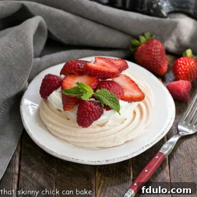 A mini pavlova on a round white plate, elegantly topped with whipped cream and fresh berries