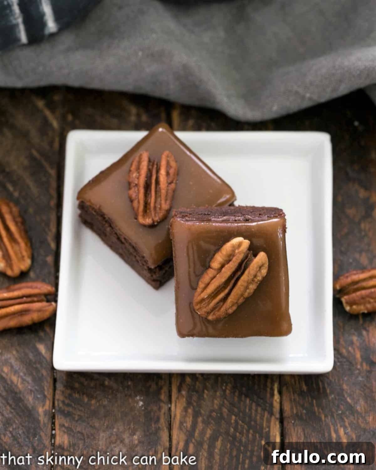 Two beautifully presented Ultimate Turtle Brownies, showcasing their thick, fudgy base, golden caramel layer, and prominent pecan halves, served on a minimalist square white plate, ready to be enjoyed as a luxurious dessert.