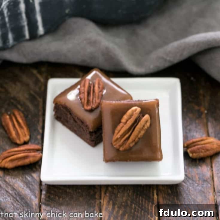 A top-down view of two rich Ultimate Turtle Brownies, each a perfect square, topped with shiny caramel and a whole pecan, presented on a minimalist square white ceramic plate, ready for serving.