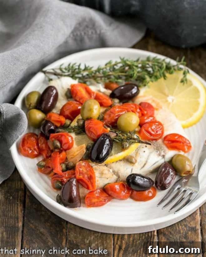 Mediterranean Sea Bass en Papillote - a healthy and delicious fish recipe cooked in parchment Mediterranean Sea Bass en Papillote on a white dinner plate with a lemon slice and thyme garnish. The fish is cooked in parchment with olives, capers, tomatoes and thyme for a healthy, tasty entree that's fun to serve!
