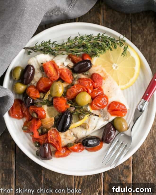 Sea Bass en Papillote - A restaurant-worthy recipe cooked in parchment with olives, capers, tomatoes and thyme for a healthy, tasty entree that's fun to serve! Overhead View of Sea Bass on a dinner plate, beautifully presented after being cooked en papillote.