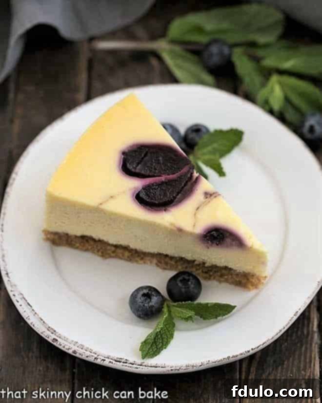 A delicious slice of Blueberry Swirl Cheesecake on a white plate, garnished with fresh mint and whole blueberries.