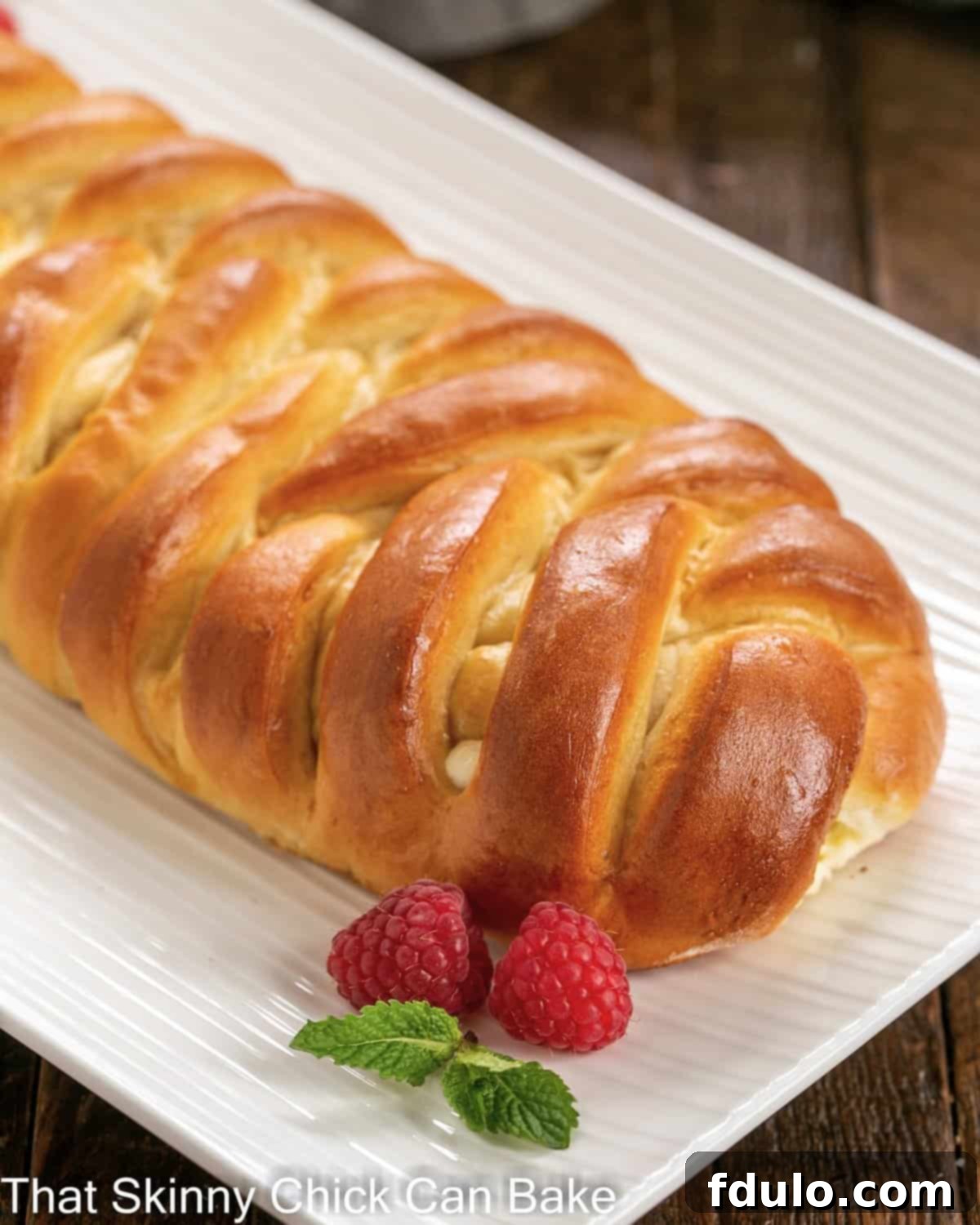 A beautifully golden-brown plaited Easter bread, generously filled with cream cheese, resting on an elegant white serving dish.