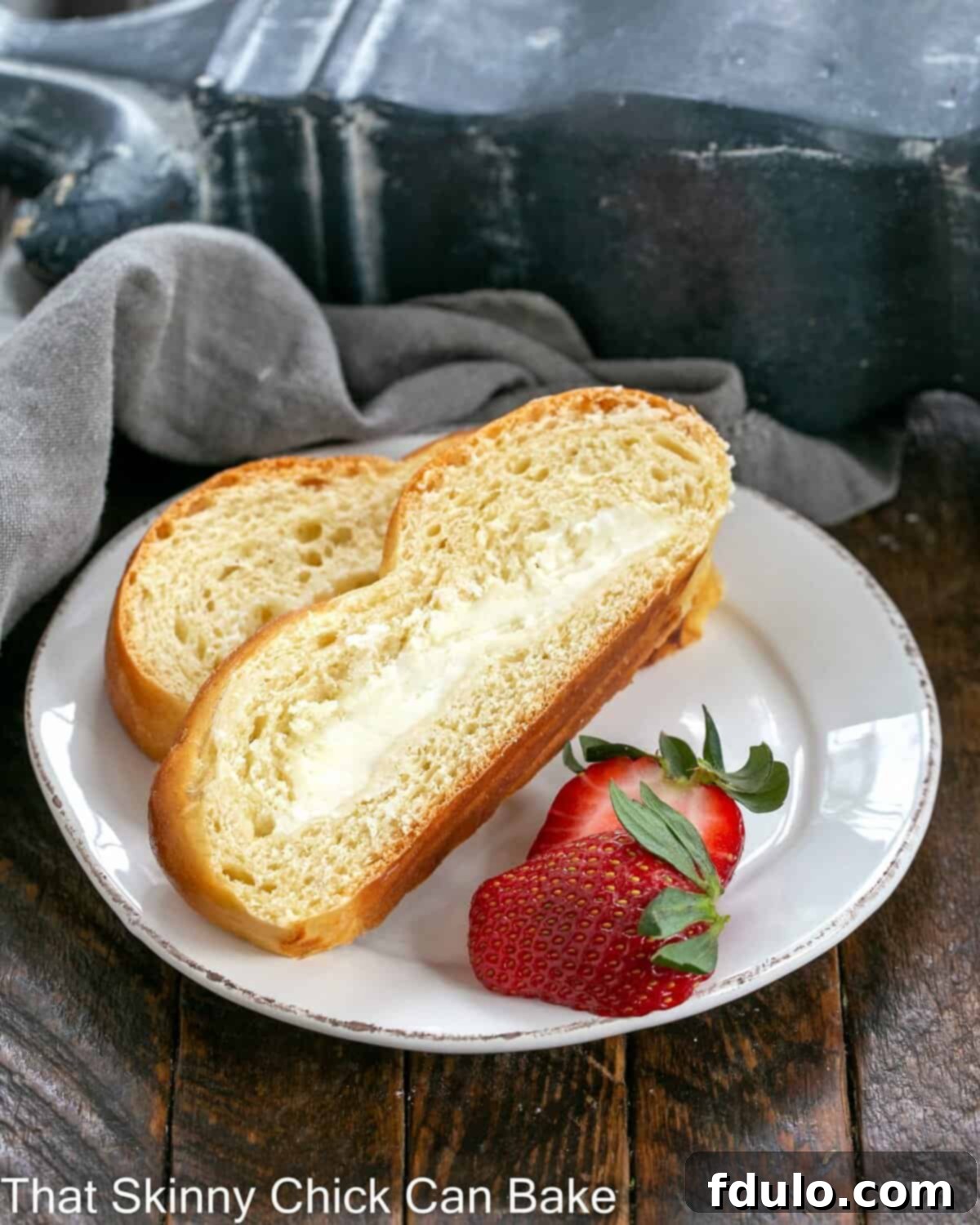 Two slices of tender, braided Easter bread with a visible cream cheese filling, garnished with fresh strawberries on a white plate.