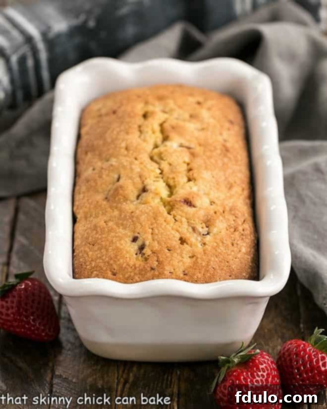 Fresh Strawberry Pound Cake - Dense, delicious, with sweet bits of fresh strawberries! A freshly baked Fresh Strawberry Pound Cake still in its white ceramic loaf pan, showcasing its golden-brown crust.