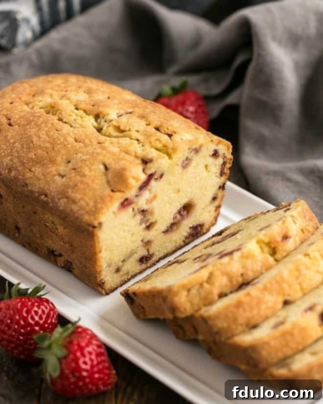 Fresh Strawberry Pound Cake - Dense, delicious, with sweet bits of fresh strawberries! A rustic image of a Fresh Strawberry Pound Cake loaf on a white ceramic tray, with half of it expertly cut into thick, inviting slices.