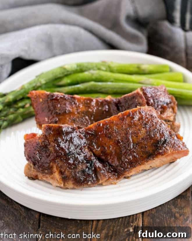 Perfectly cooked Oven Baked Ribs served on a white plate with fresh asparagus spears.