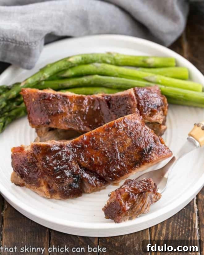 A tender bite of rib meat on a fork, lifted from a plate with two ribs and asparagus, showcasing its succulence.
