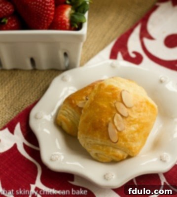 Homemade Almond Croissants - made from scratch, these exquisite croissants taste like they're from a French bakery! Two almond topped Homemade Almond Croissants on a white ceramic plate.