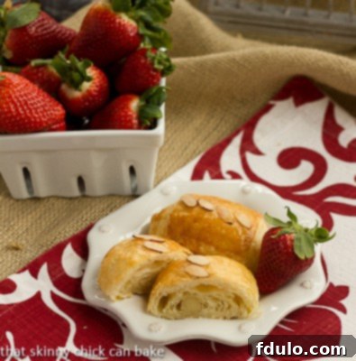 Homemade Almond Croissants - made from scratch, these exquisite croissants taste like they're from a French bakery! Almond croissants on a white plate on a red and white napkin with a bowl of fresh strawberries.