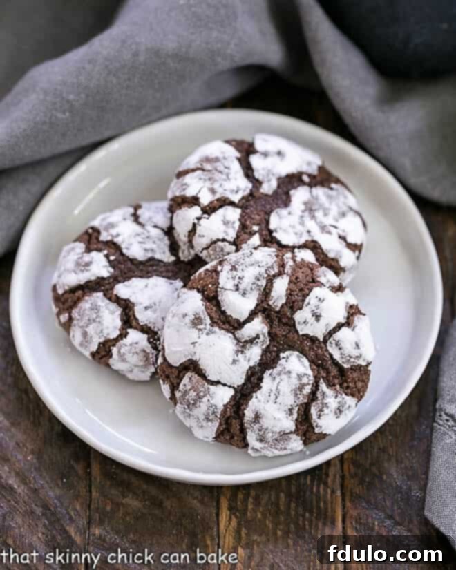 Overhead view of 3 chocolate earthquake cookies on a round white plate, showcasing their cracked powdered sugar coating and rich dark centers.