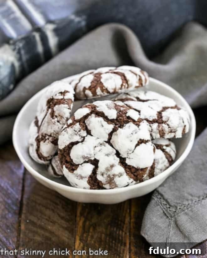 A beautiful white ceramic bowl brimming with freshly baked chocolate earthquake cookies, highlighting their distinct powdered sugar coating and deep cracks.