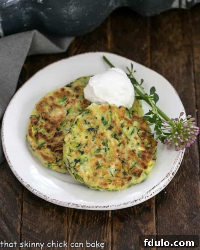 Three golden-brown zucchini fritters neatly arranged on a white plate, garnished with fresh herbs and a dollop of sour cream, showcasing their tender interior and crispy exterior.