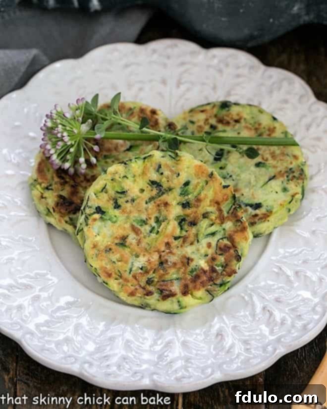 Overhead view of three golden-brown zucchini fritters, garnished with delicate herbs, presented on an elegant white decorative plate, ready for serving.