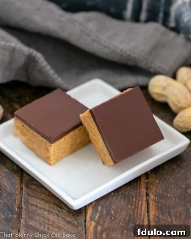 Two perfectly sliced Better Than Reese's Peanut Butter Bars displayed on a square white plate, highlighting their distinct layers.