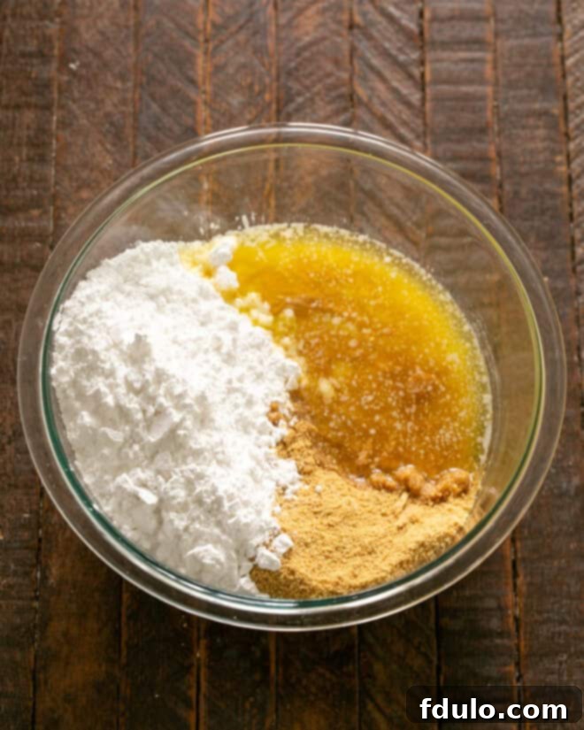 Step 2: Adding powdered sugar, graham cracker crumbs, peanut butter, and melted butter to a mixing bowl.