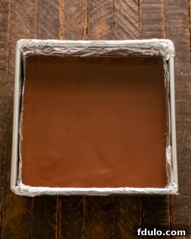 Step 6: Spreading the melted chocolate topping smoothly over the chilled peanut butter layer in the pan.