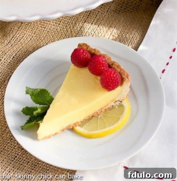 A slice of Tarte au Citron AKA French Lemon Tart garnished with raspberries.