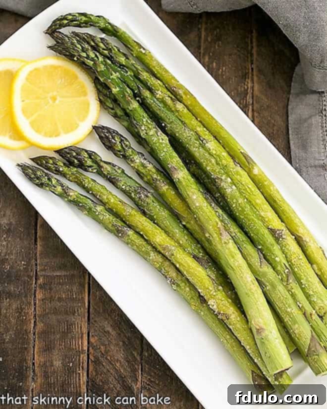 Overhead view of Easy Oven Roasted Asparagus on a white tray with lemon slices.