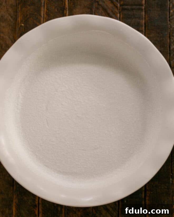 Luscious Peach Clafoutis 3 A ceramic baking dish being buttered and sugared, preparing it for the clafoutis batter.