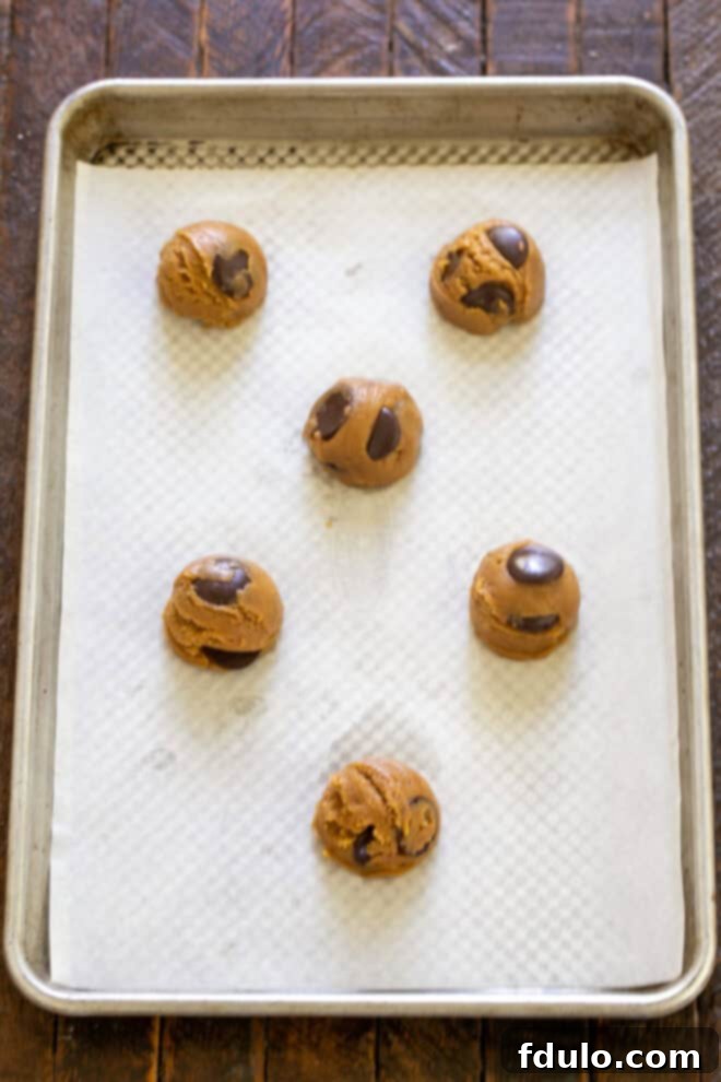 Next-Level Brown Butter Chocolate Chip Cookies 8 Scooped cookie dough balls arranged on a parchment-lined baking sheet.