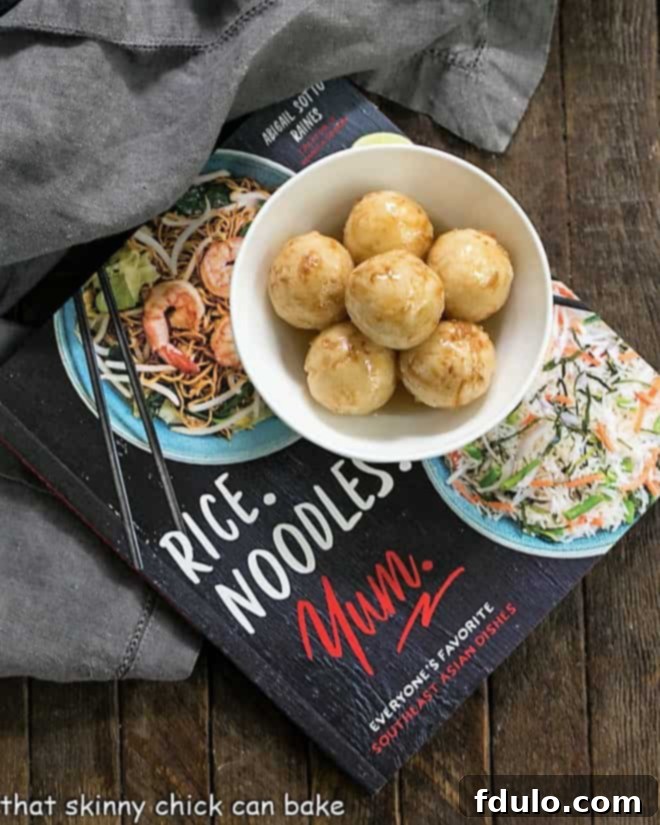Carioca or Fried Sticky Rice Balls - a Filipino treat with a triple dose of coconut including the drizzle of decadent coconut caramel sauce! A collection of Carioca, or Fried Sticky Rice Balls, beautifully presented in a white ceramic bowl, resting on top of the 'Rice.Noodles.Yum' cookbook, emphasizing their connection to authentic Southeast Asian cuisine.
