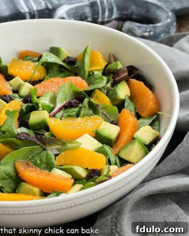Vibrant Cherry Orange Salad with Citrus Vinaigrette in a white serving bowl, showcasing fresh greens, ruby red dried cherries, and creamy avocado cubes.