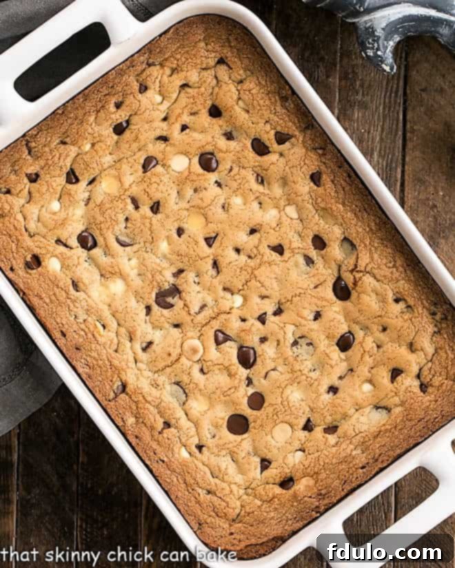 An overhead view of freshly baked chocolate chip cookie bars cooling in a white ceramic baking pan, showcasing their golden-brown edges and soft centers.