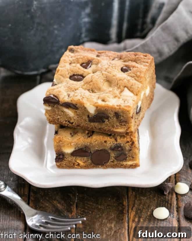 Two perfectly baked chocolate chip bars stacked on a delicate white dessert plate, with a silver fork resting beside them, ready to be enjoyed.