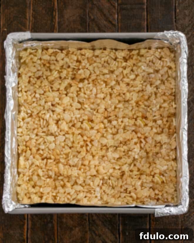 Peanut Butter Chocolate Krispie Dream Bars 6 Image showing the Rice Krispies mixture being pressed evenly into the bottom of a prepared baking pan.