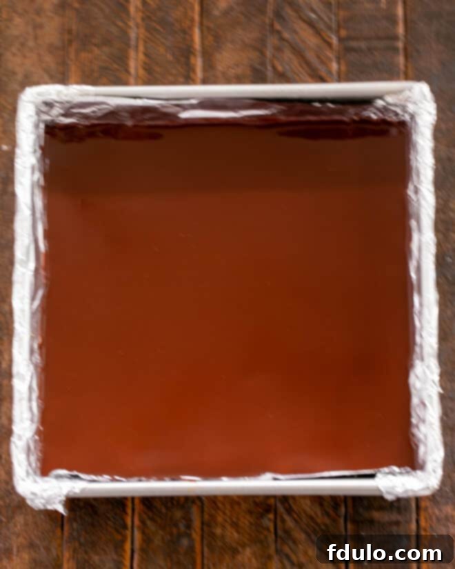 Peanut Butter Chocolate Krispie Dream Bars 8 Image showing the final dark chocolate layer being poured and spread over the peanut butter layer, followed by chilling.