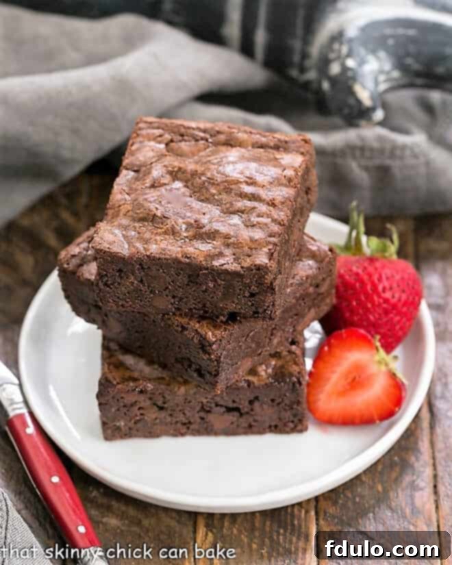 A stack of 3 homemade sheet pan brownies on a small white plate, showcasing their rich, dark interior and shiny crust.